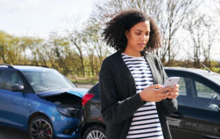 Female Driver Contacting Car Insurance Company On Mobile Phone After Road Traffic Accident